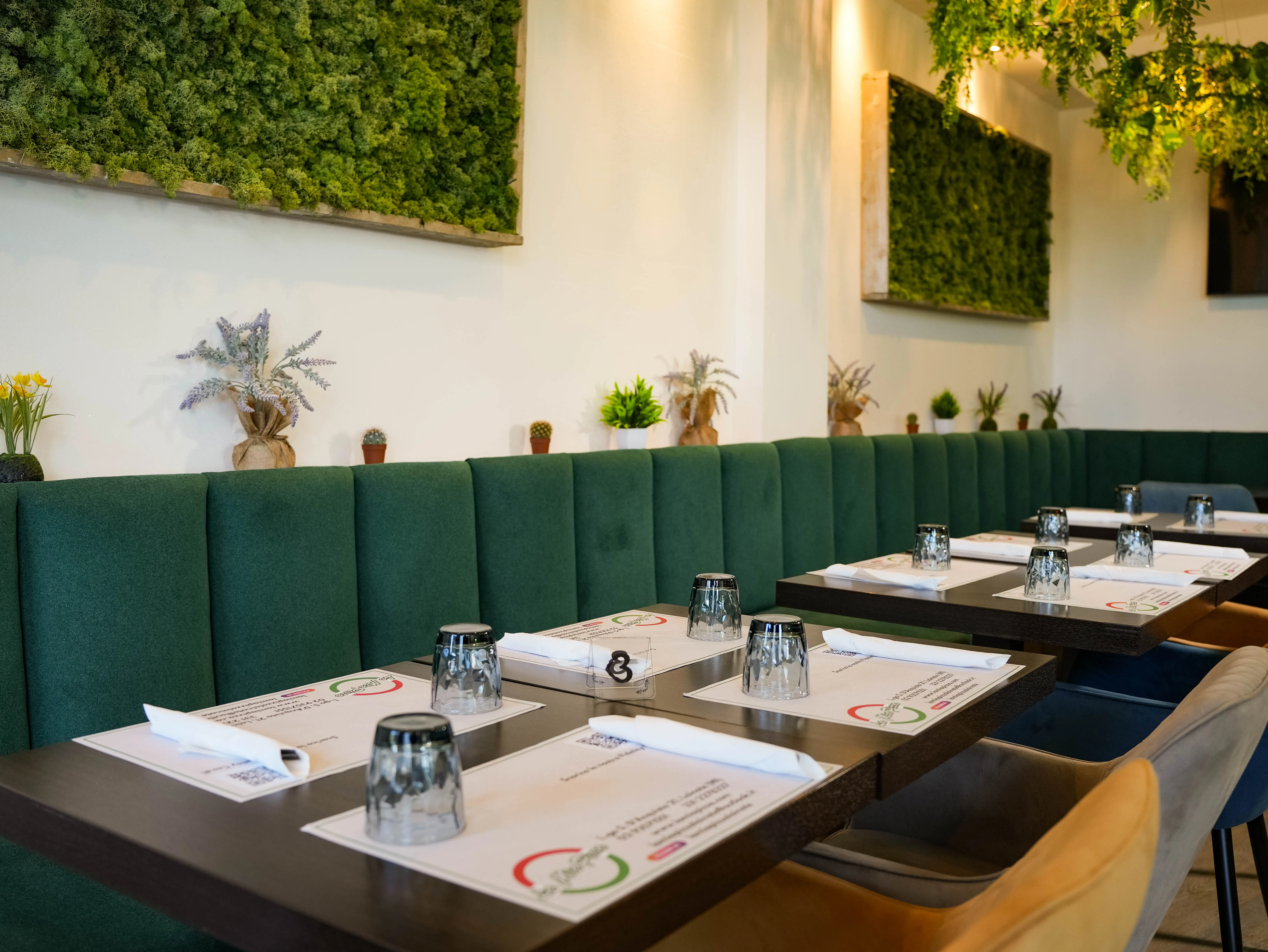 La sala interna della pizzeria con banchetta in velluto verde smeraldo, pannelli di muschio stabilizzato incorniciati alle pareti e lampadari floreali sospesi